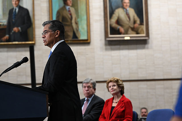 Secretary Becerra in a dark colored suit standing at a podium. 