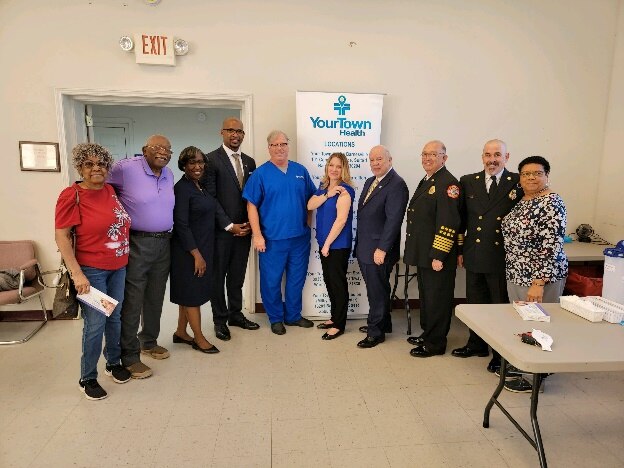 Deputy Andrea Palm is wearing a blue blouse and black slacks standing to her right is a health care worker wearing blue scrubs.