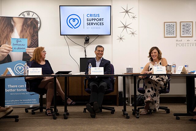 Secretary Becerra is seated at conference table wearing a dark suit. To the right of him is a lady wearing a light color dress