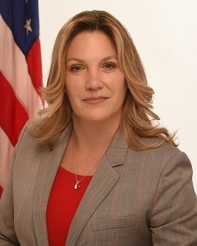 Deputy Secretary Andrea Palm seated in front of the American Flag wearing a grey blazer and red top.