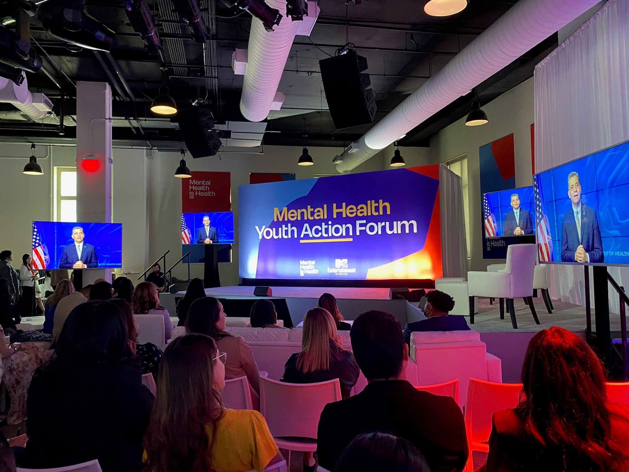 People sitting in room, screen says “Mental Health Youth Action Forum.