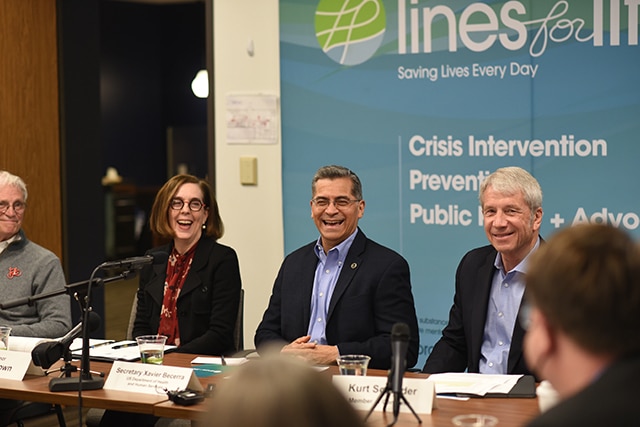 Congressman Earl Blumenauer, Oregon Governor Kate Brown, Secretary Xavier Becerra, and Congressman Kurt Schrader smiling while sitting at a long table during a roundtable event.