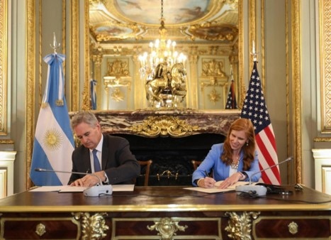 Minister Pablo Quirno and Director Bethany Kozma, Secretary’s Office of Global Affairs sitting at a desk in a room, each signing documents. The flags of Argentina and the United States behind them.