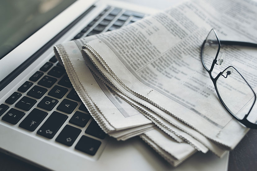 A folded newspaper and a pair of eyeglasses resting on the keyboard of an open laptop.