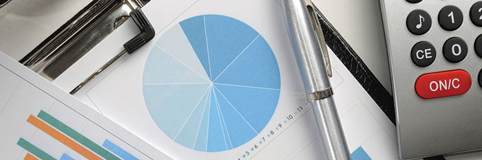 Close up photo of a desktop with a clipboard with a pie chart, silver pen, and a calculator