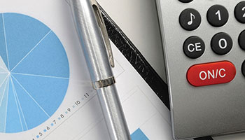 Close up photo of a desktop with a silver pen, a calculator and a pie chart.