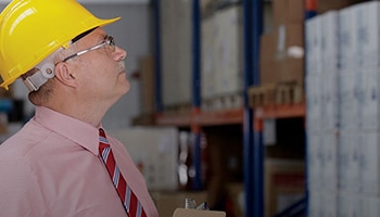 Man with a yellow hard hat looking in a warehouse at boxes.