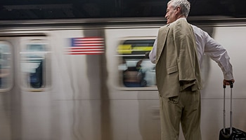 A man with a rolling suitcase standing in front of a speeding subway train.