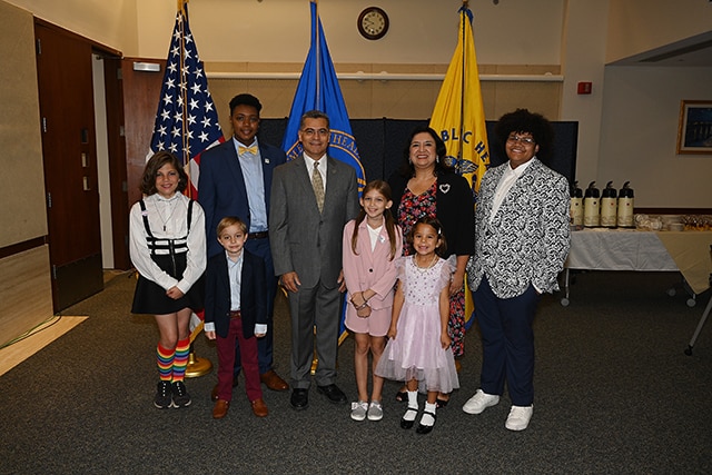 Secretary Becerra with a group of trans youth photographed in front of the American flag, HHS flag and Public Health Service flag.