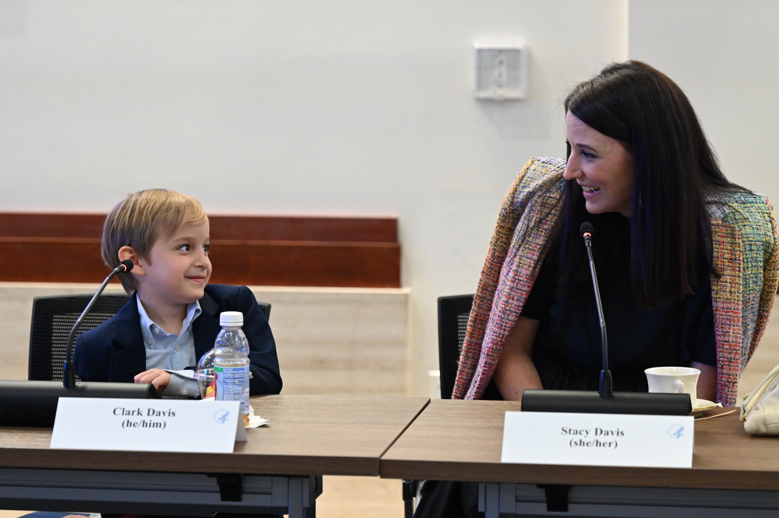 Young child smiling looking towards parent in front of microphones during round table event