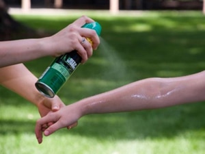 A mother is in the process of correctly applying mosquito repellant spray to her daughter’s right forearm.