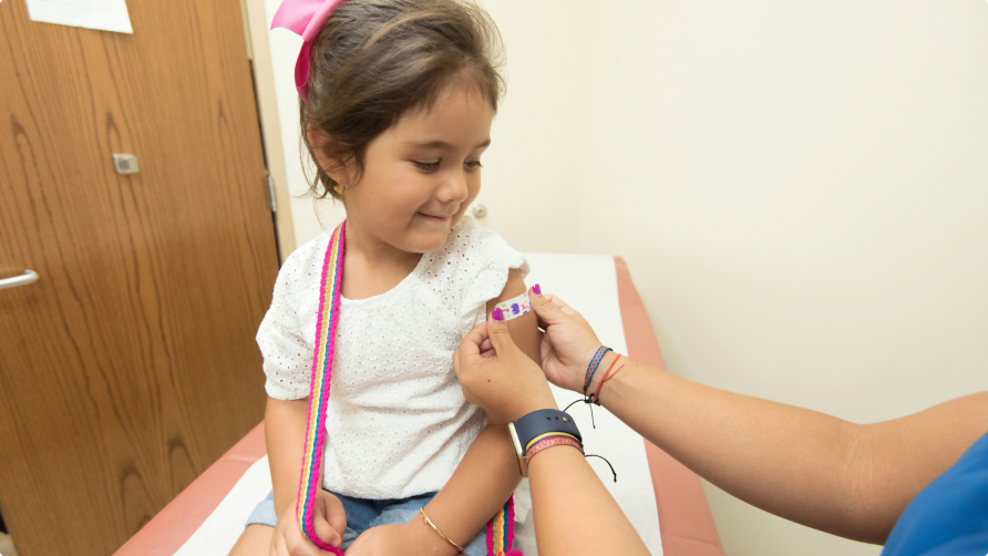 A little girl at the doctor's office getting a bandaid after getting a vaccine shot